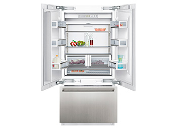 Frigorífico grisáceo de la marca Siemens sobre un fondo blanco. Es de dos puertas y estas están abiertas, permitiendo ver el interior del frigorífico. La puerta del congelador es tipo cajón y también está abierta.